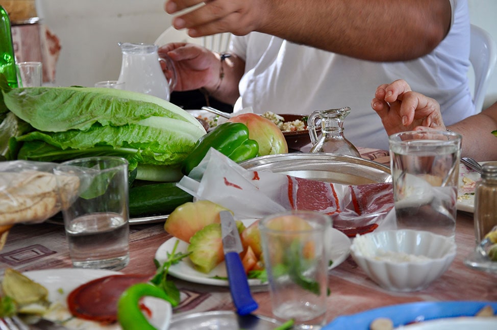 A Lebanese lunch table filled with vegetables, meats, plates and drinks.
