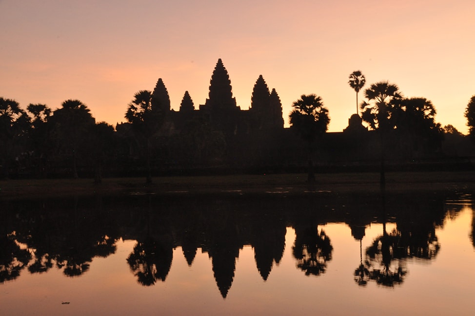 Silhouette of Angkor Wat against a pink sky at sunrise