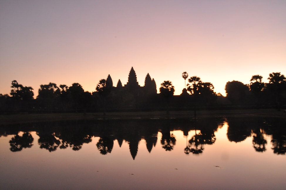 The sky goes from black to blue to pink as the sun rises over Angkor Wat