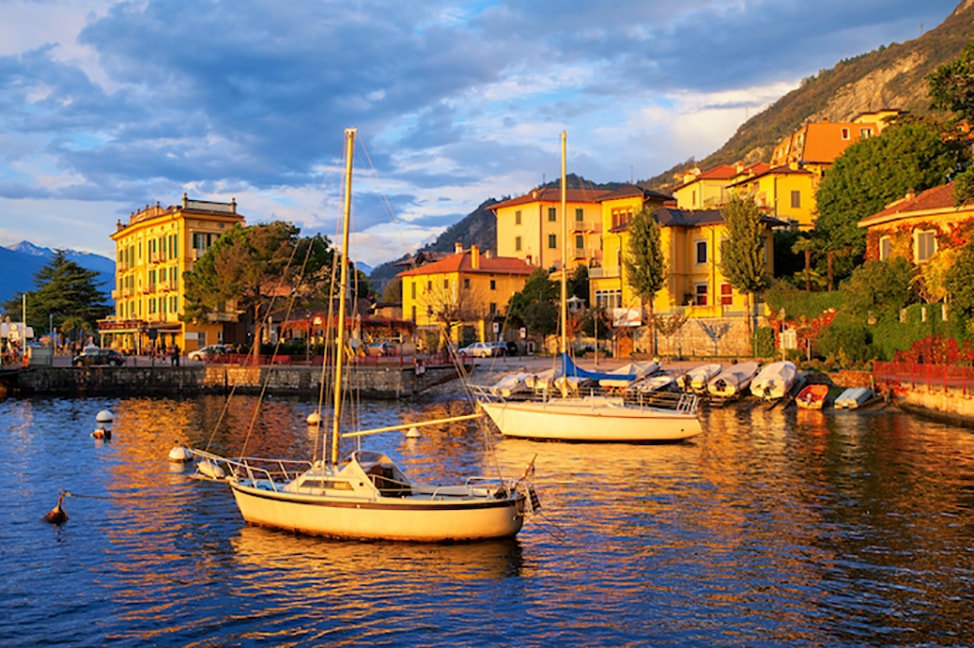 A golden light falls on the buildings and boats along the coast of Lake Como