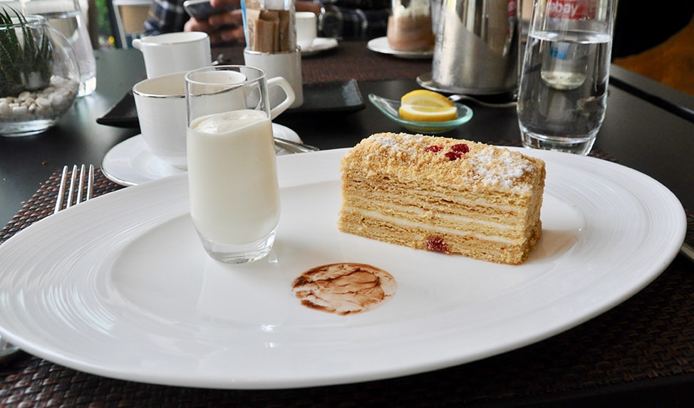 A piece of Honey Cake is accompanied by a glass of cream to use as a topping