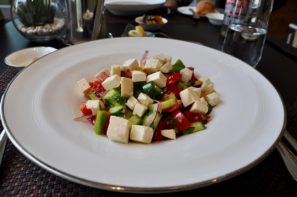 White plate with a salad of cubed tomatoes, cucumbers, onions and cheese