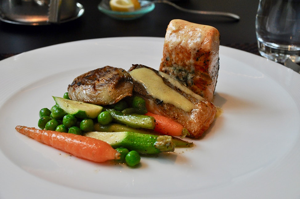 A large white plate holds pieces of roasted salmon and fresh vegetables 