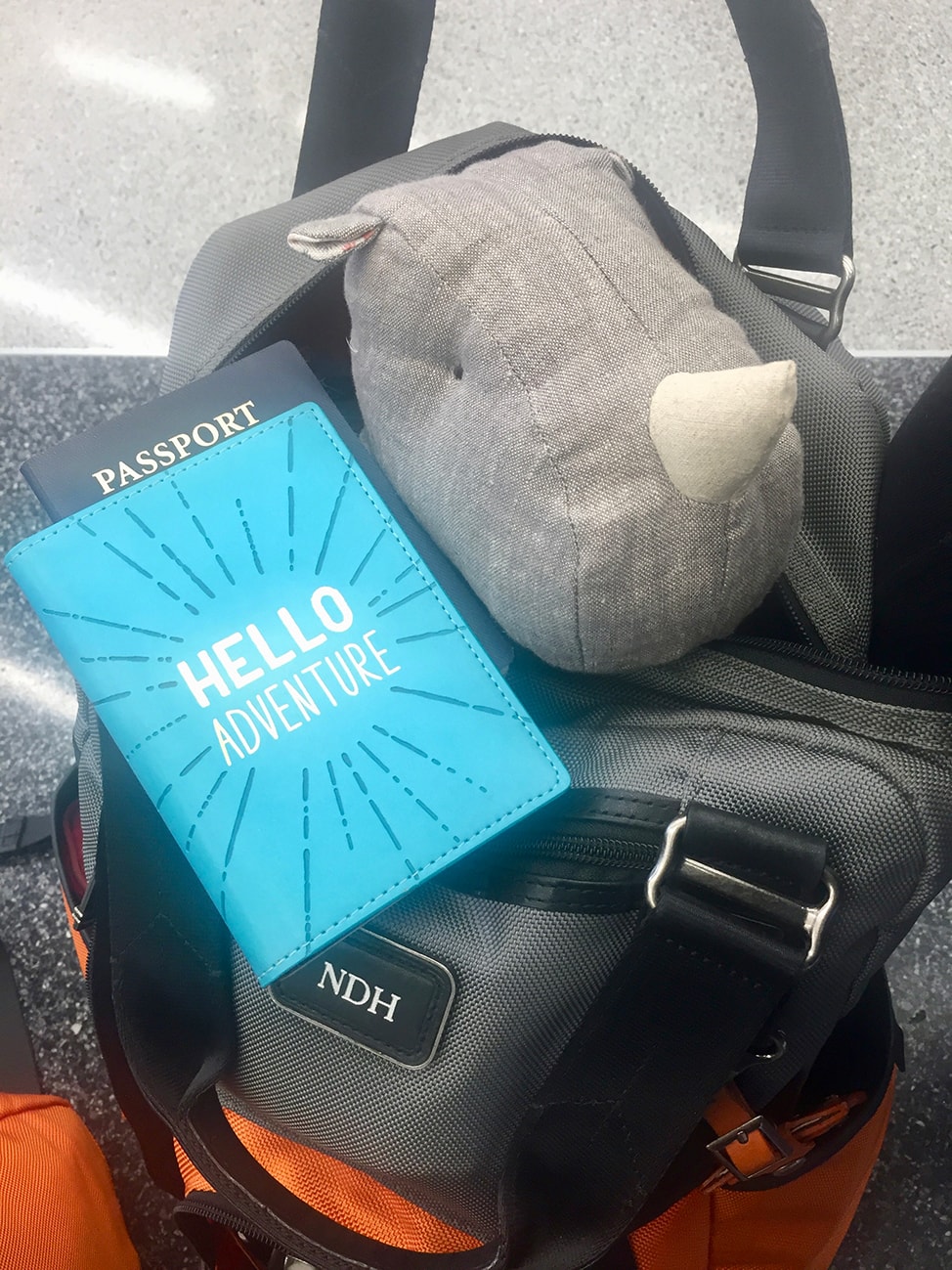 Orange and gray Tumi backpack with a stuffed rhino and passport
