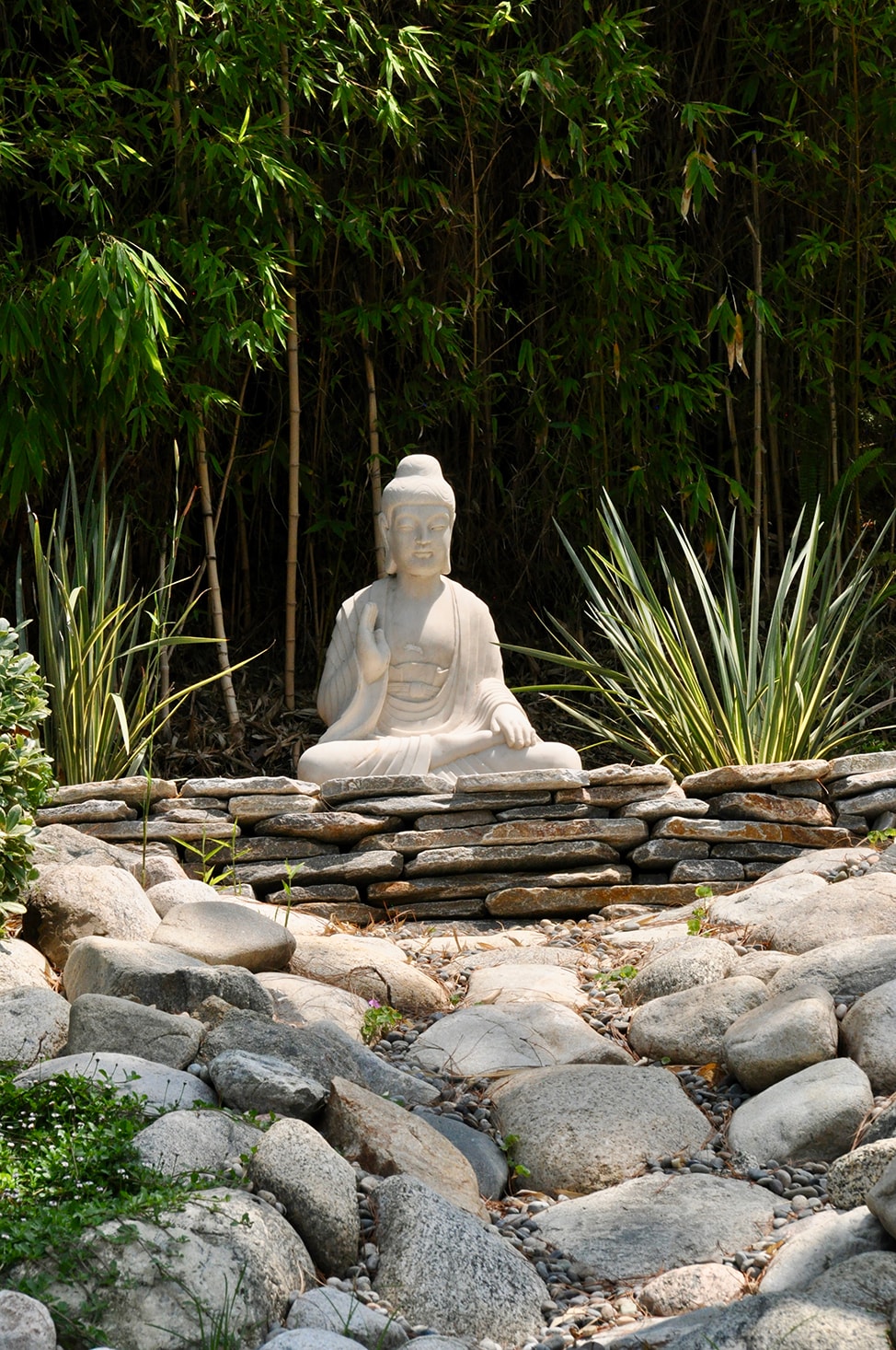 A white stone statue of the Buddha sits atop a slate rock wall.