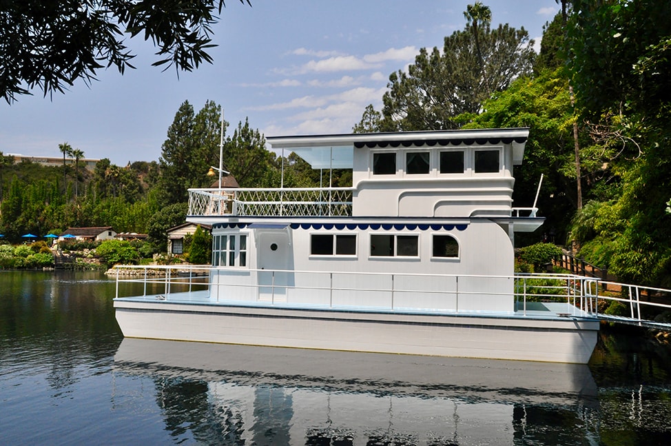 A white house boat docked along the side of the lake.