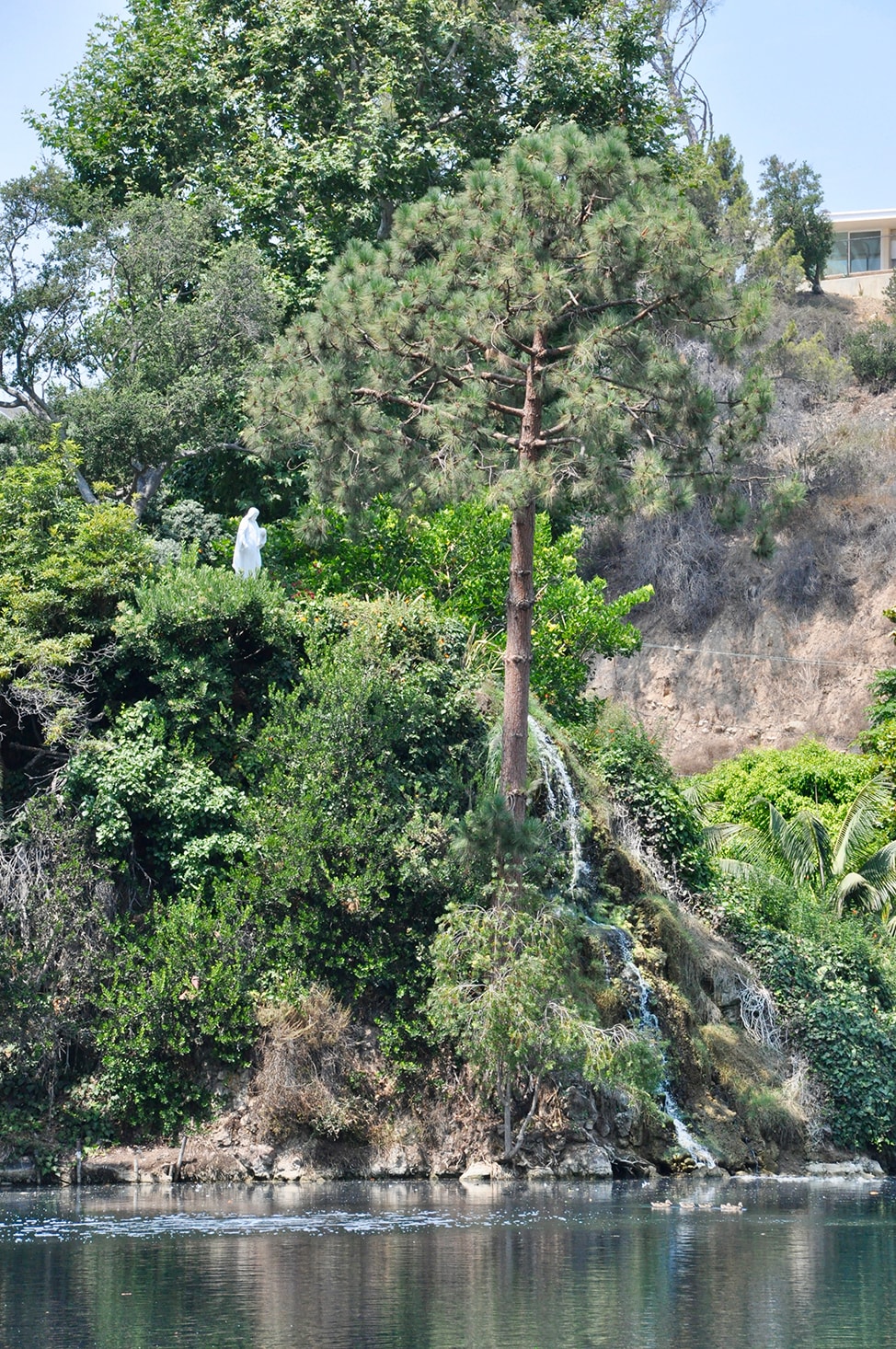 A statue of Jesus Christ stands on a green hillside with a waterfall trickling toward the lake.