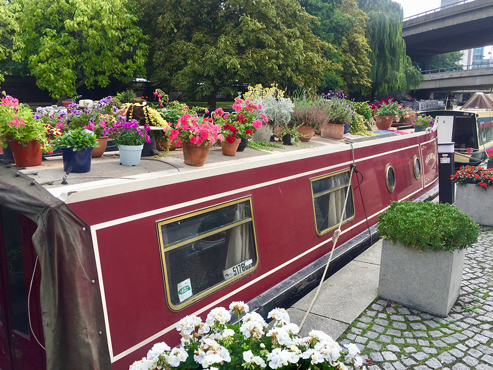 Red houseboat in Maida Vale with potted flowers and plants on the roof.