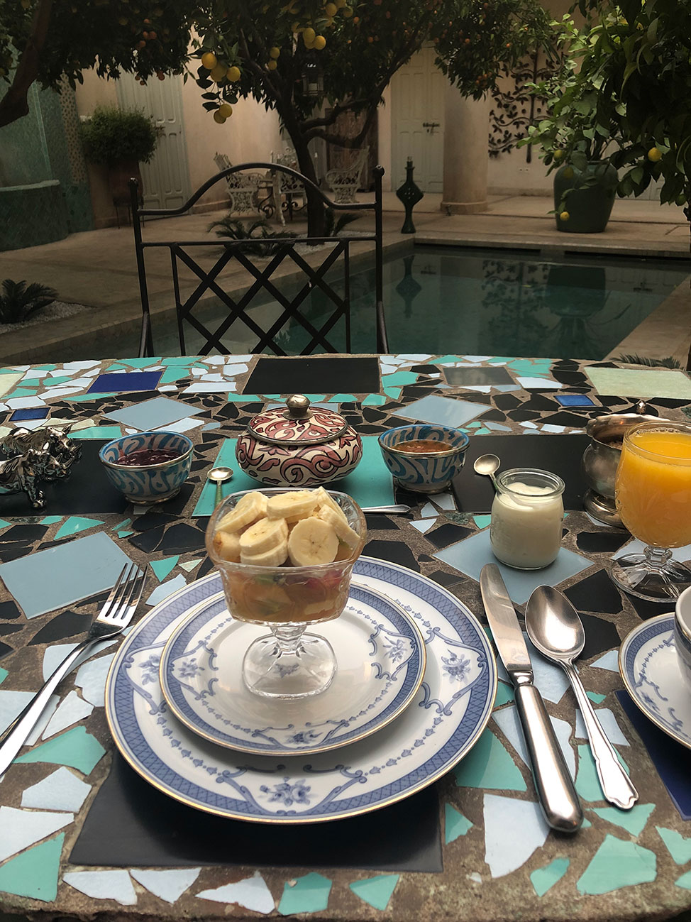 Breakfast place setting on a blue mosaic table overlooking the courtyard's pool.