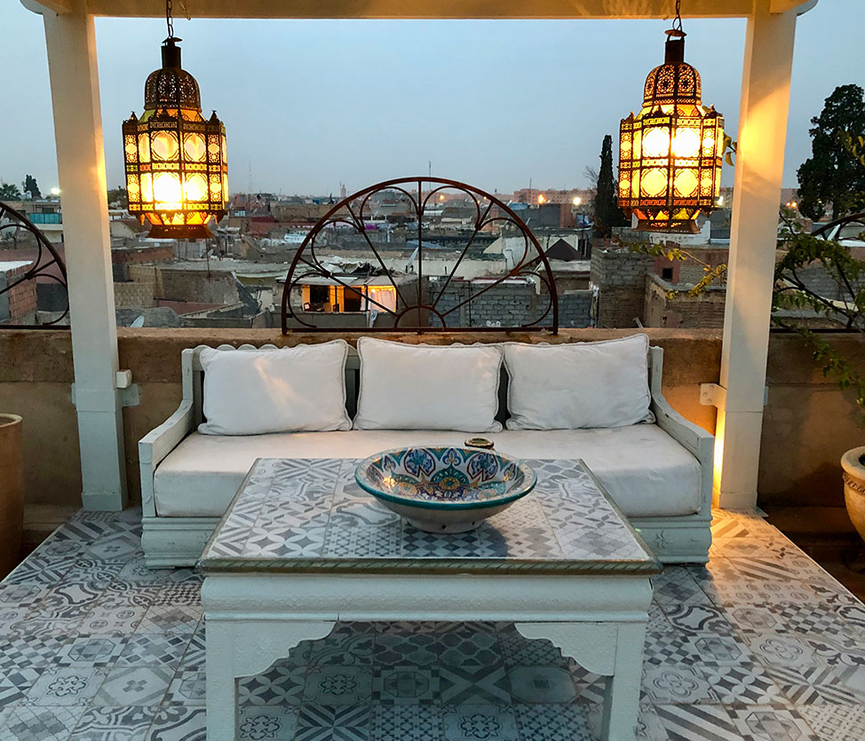Rooftop seating area with hanging lanterns, a while couch and tiled table and floor