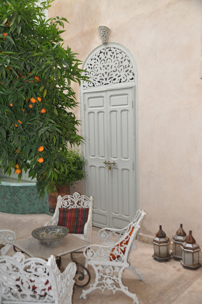 Seating Area with white iron chairs and an orange tree in front of a light blue wooden door