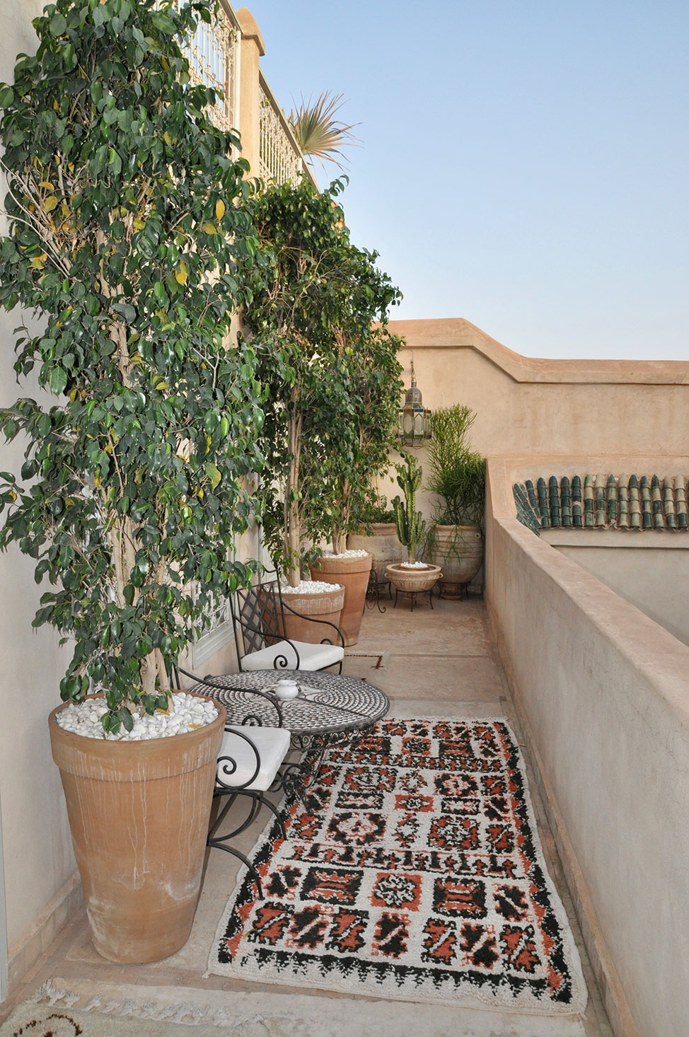 Outdoor seating area at with potted plants, Moroccan rug and wrought iron furniture.
