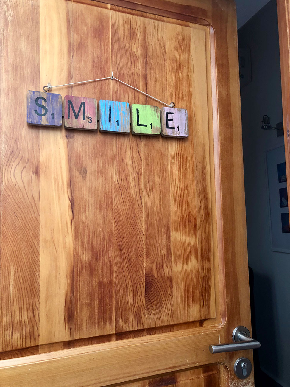 A hotel room door with wooden Scrabble tiles that spell out the name Smile. 