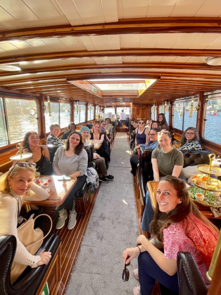 A group of women sitting on a long river boat and smiling at the camera.