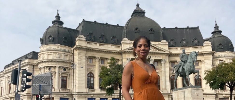 The author, a solo traveler, in an orange dress standing in front of an ornate building in Bucharest, Romania.
