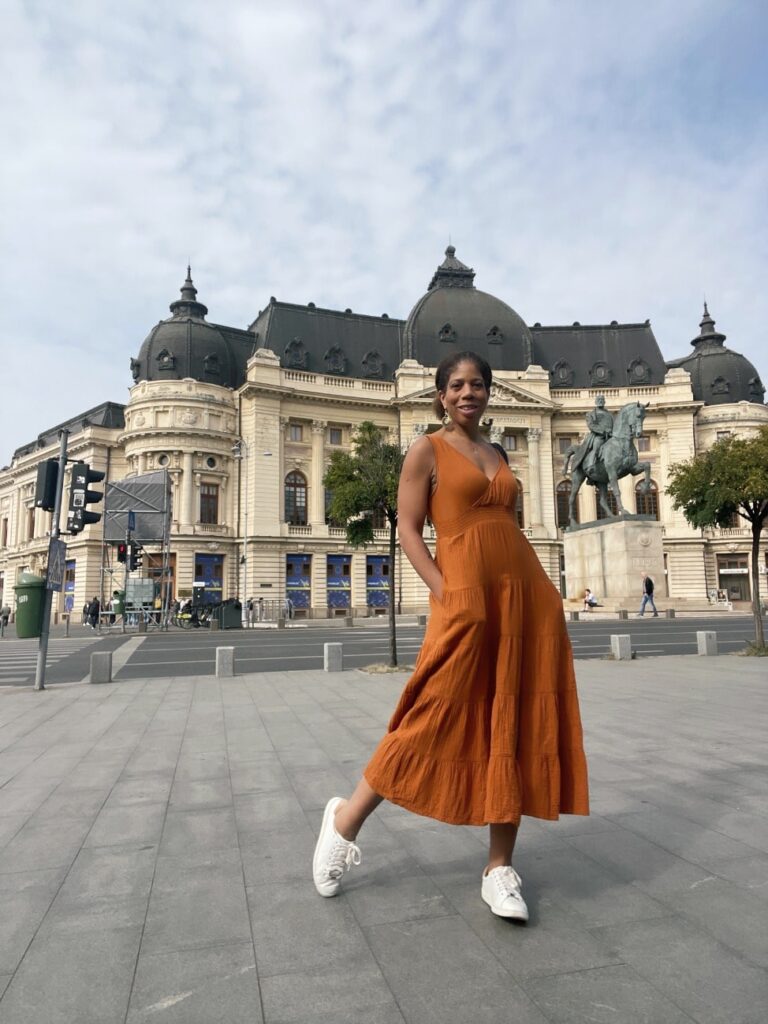 The author, a solo traveler, in an orange dress standing in front of an ornate building in Bucharest, Romania.